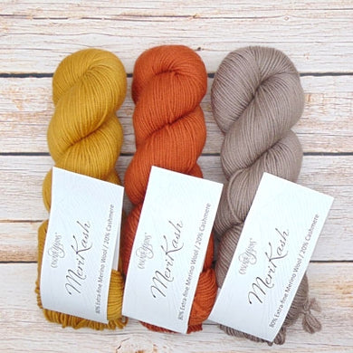 Three skeins of yarn in yellow, orange, and brown with merino and cashmere for knitting.